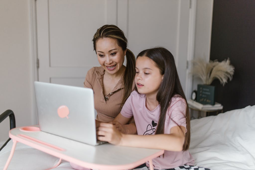 Homepage Asian woman and young girl learning on a laptop at home, engaged in online education.